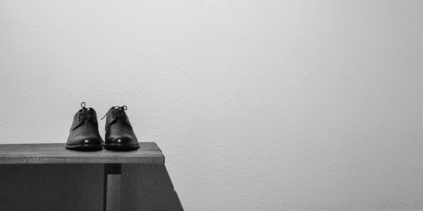 Pair of black leather shoes on a concrete block against a white wall