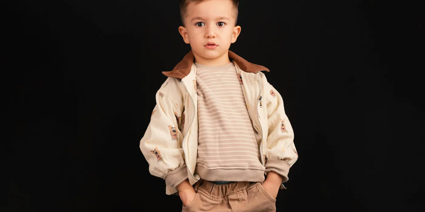 Young boy in a cream jacket and striped top on a dark studio background