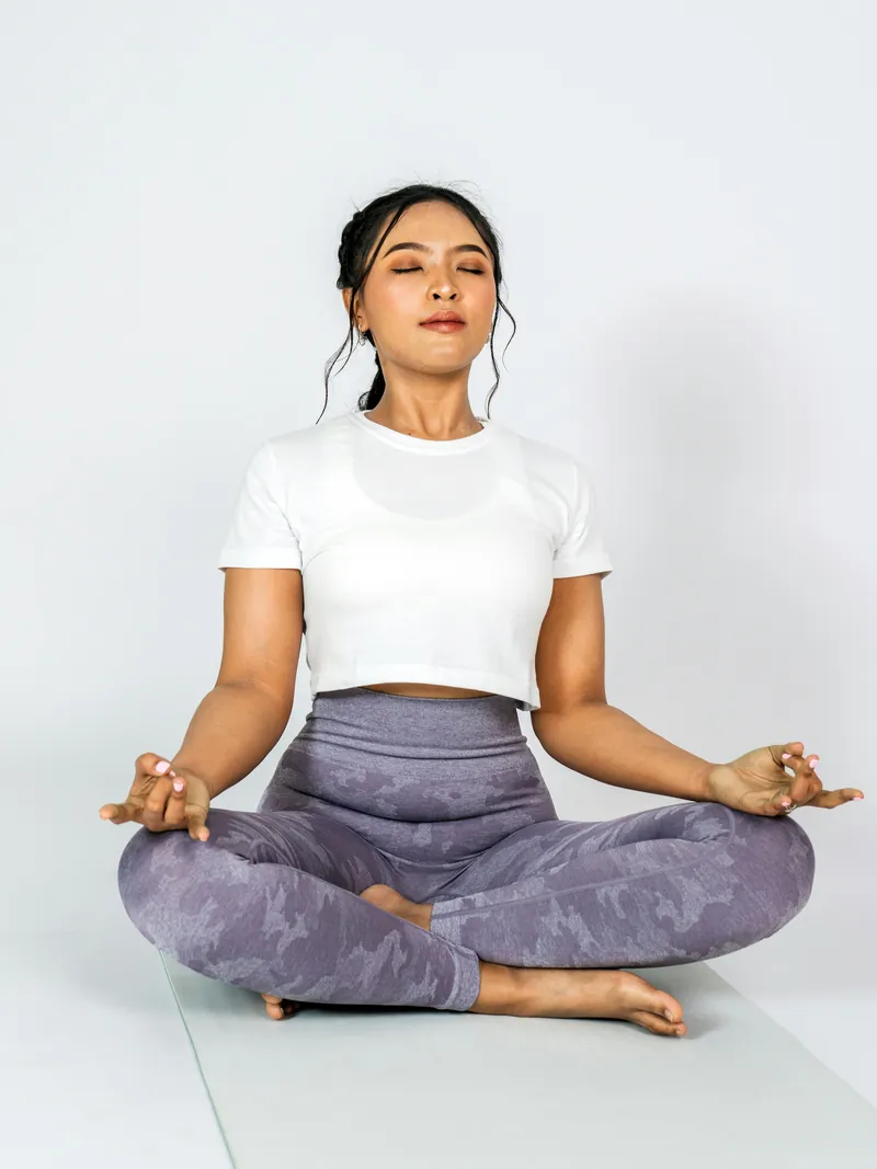Model seated cross-legged in lavender printed yoga leggings and a white tee