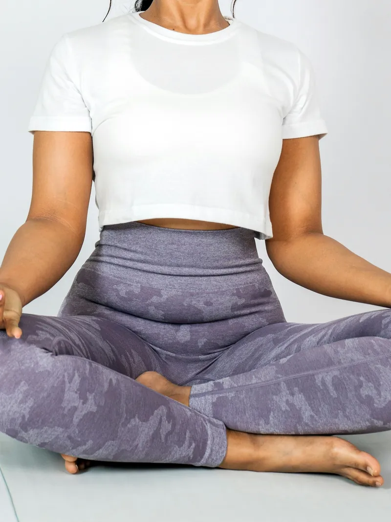 Model seated cross-legged in lavender printed yoga leggings and a white tee