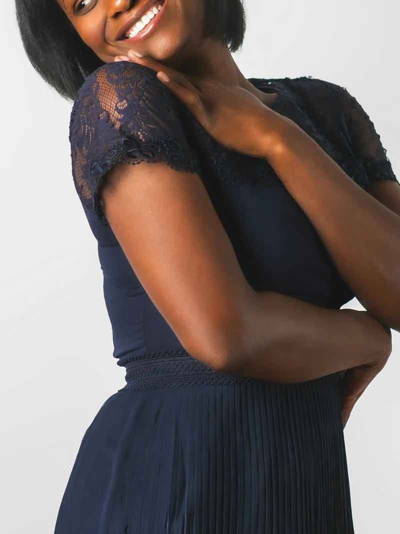 Model in a navy midi dress with lace sleeves and a pleated skirt