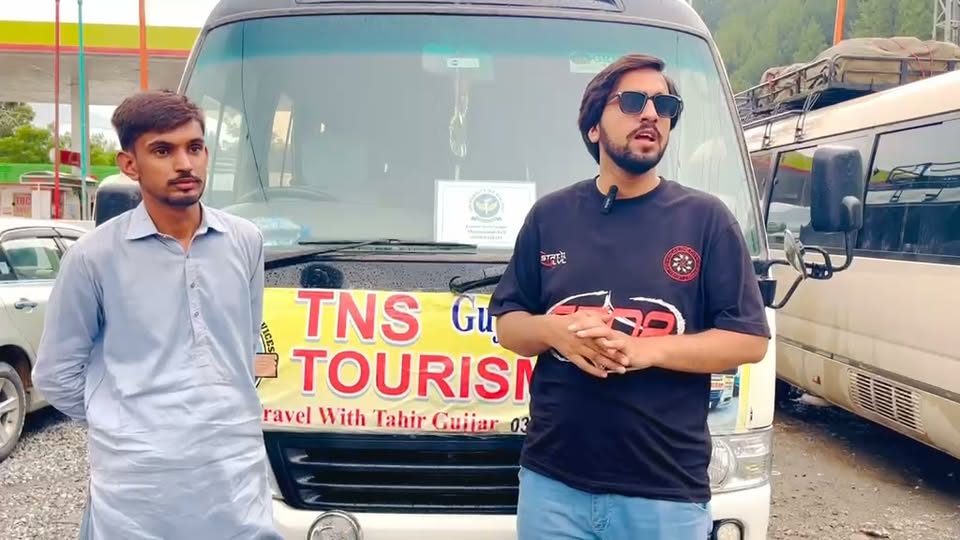 Two members of the TNS team standing beside the branded coaster at a roadside fuel station